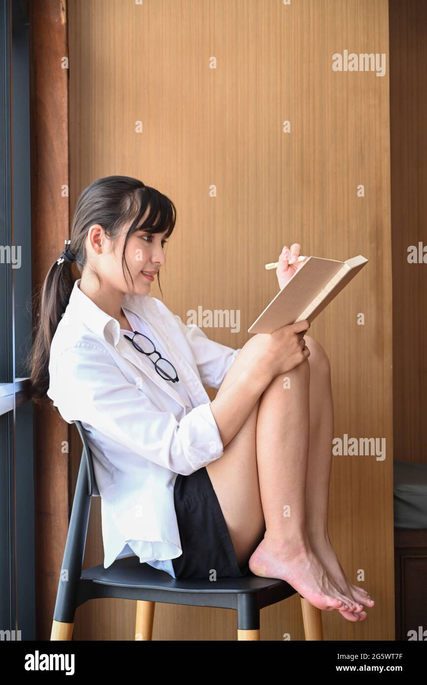 Young female sitting on chair and reading book Stock Photo - Alamy