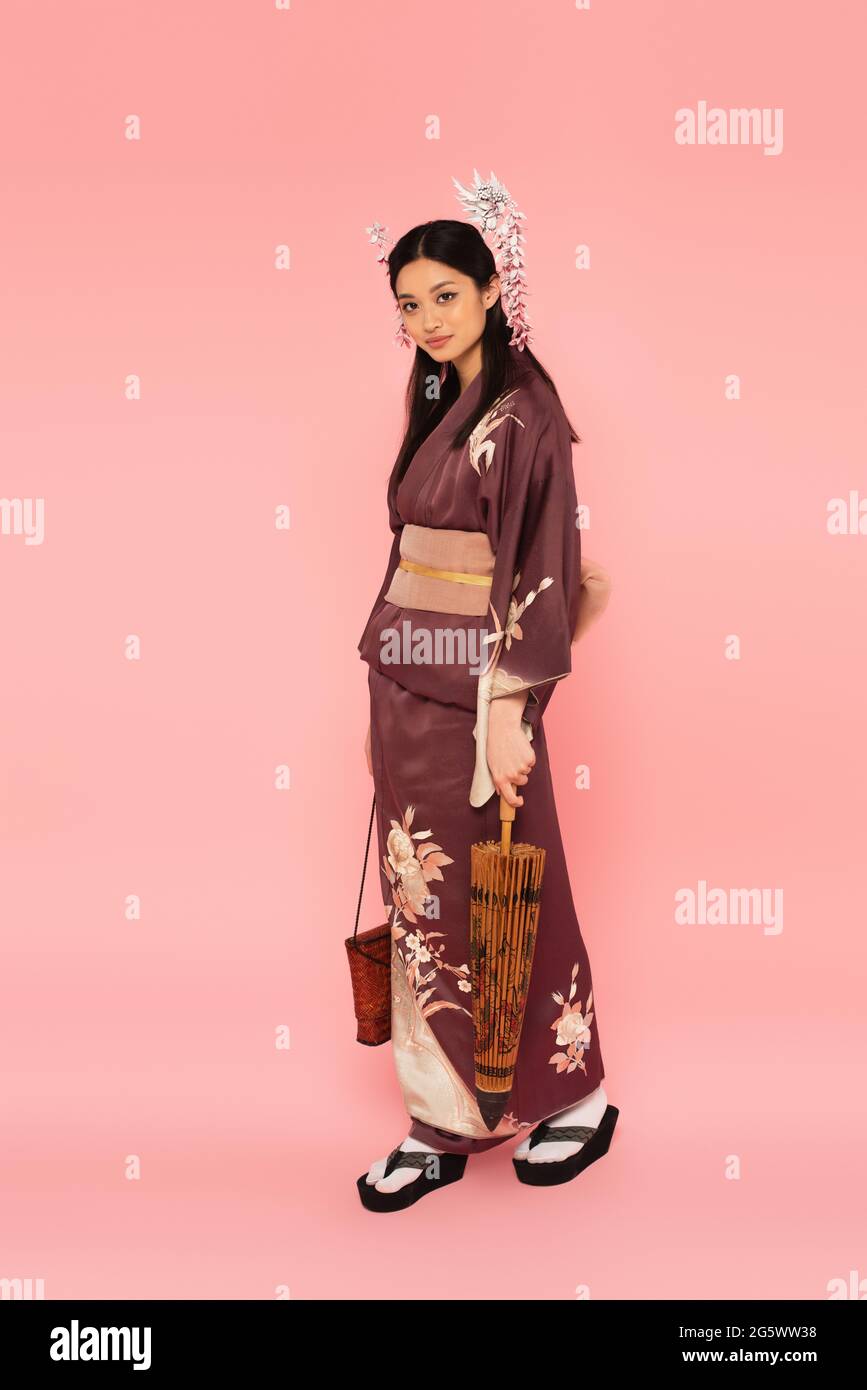 Asian woman with handbag and umbrella standing on pink background Stock Photo