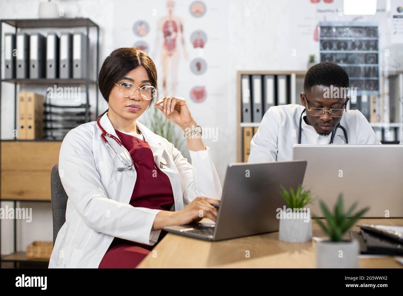 Multiracial colleagues in medical white coats working on laptops and ...