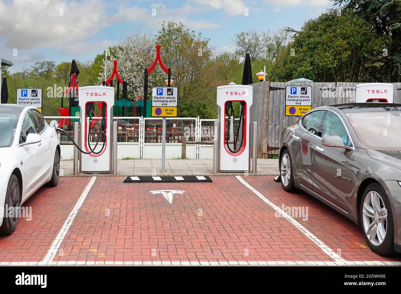 Electric cars connected to Tesla supercharger stall in parking bays at Welcome Break facility on M42 motorway service station Alvechurch Birmingham UK Stock Photo
