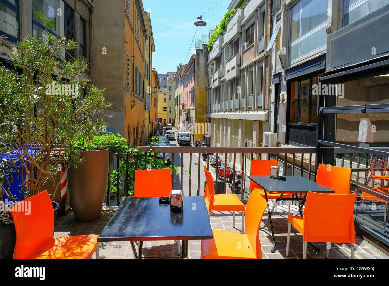 Black table with orange chairs across plants, colorful buildings in a restaurant terrace. Street cafe exterior. City life Stock Photo
