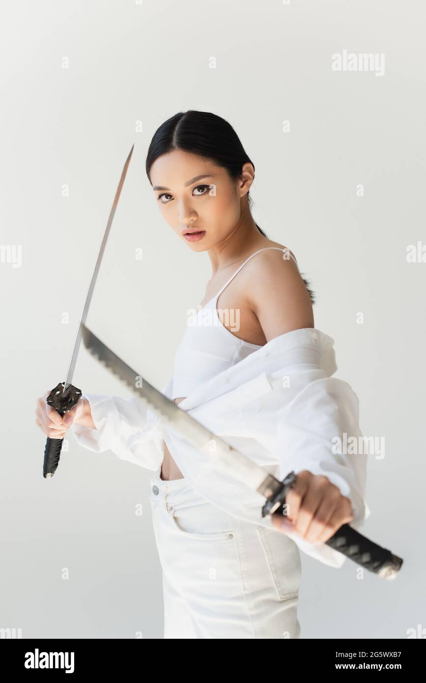 Pretty japanese woman with blurred swords standing isolated on grey Stock Photo