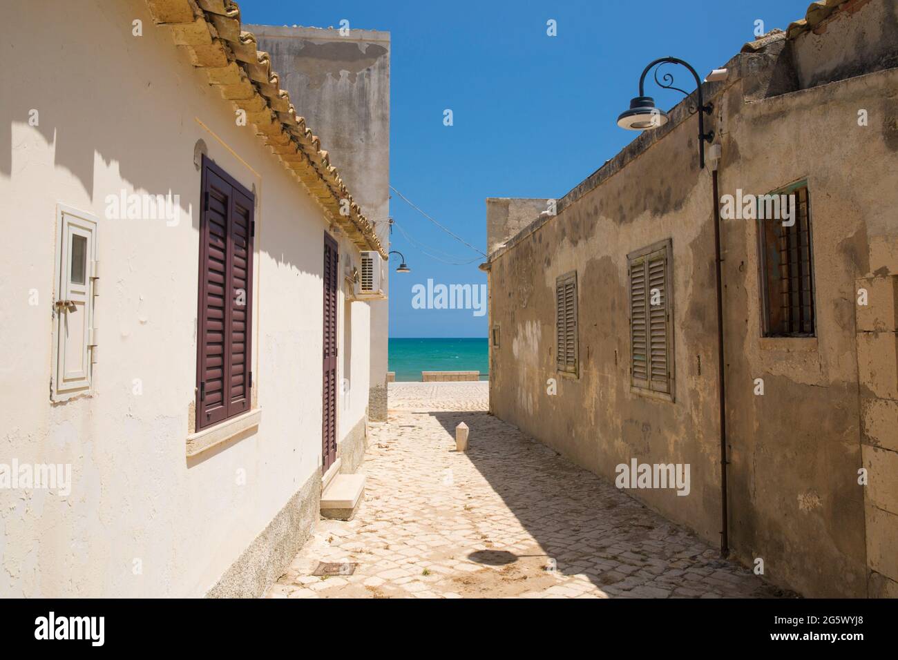 Sampieri, Ragusa, Sicily, Italy. Narrow lane between traditional fishermen's houses, the turquoise waters of the Mediterranean Sea beyond. Stock Photo