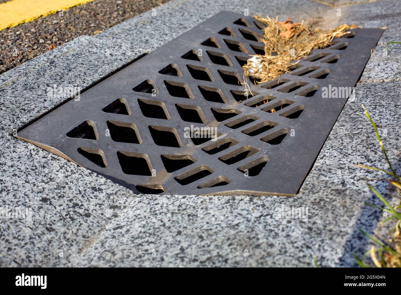 grate with holes for drainage of storm water from a concrete ditch on the side of an asphalt road close-up of a dirty drain canal. Stock Photo