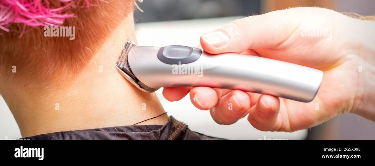 Back view of hairdresser's hand shaving nape and neck with electric trimmer of young caucasian