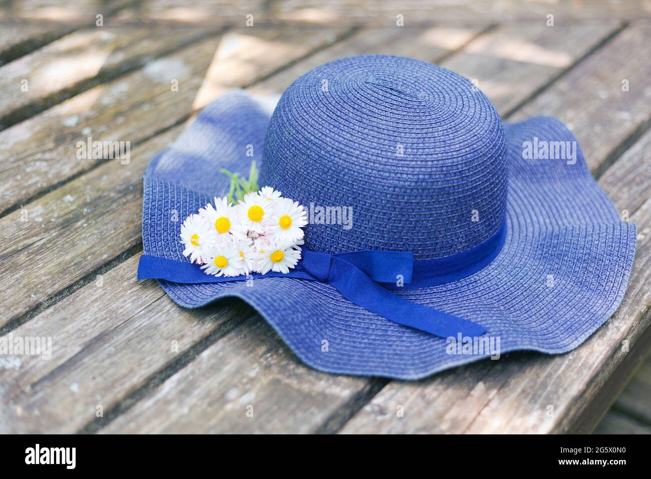 blue hat lying on a wooden bench with small daisies bouquet. bouquet of meadow and wild flowers. A romantic photo of a cute summer time. vacation Stock Photo
