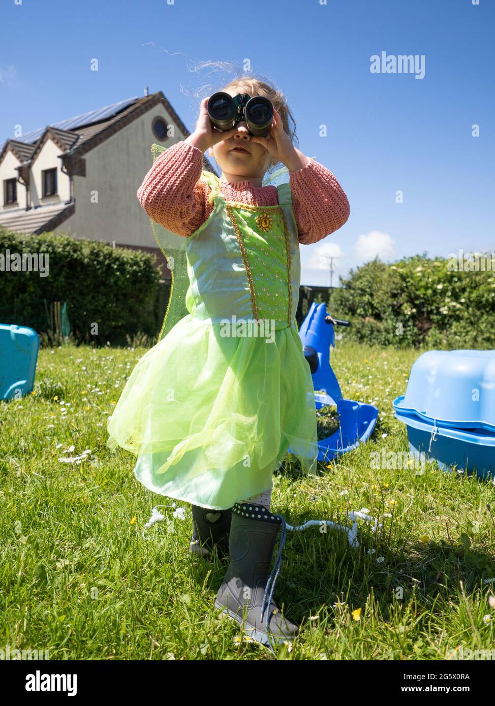 Young girl dressed as a fairy looking through binoculars, Cornwall, UK Stock Photo