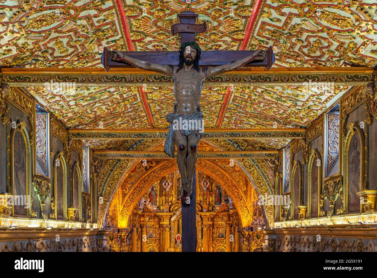 Jesus Christ on cross sculpture with gold leaf baroque style interior of San Francisco church convent, Quito, Ecuador. Stock Photo