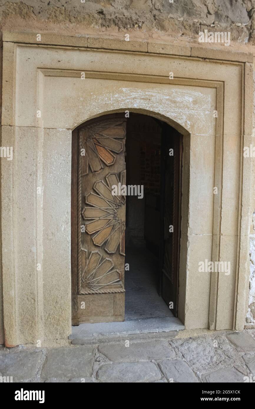A half-open double-leaf old wooden door in a pattern. It is installed in a stone castle Stock Photo
