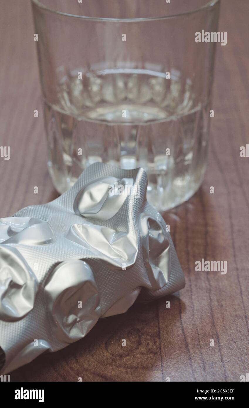 crumpled pill blister pack and glass of water Stock Photo