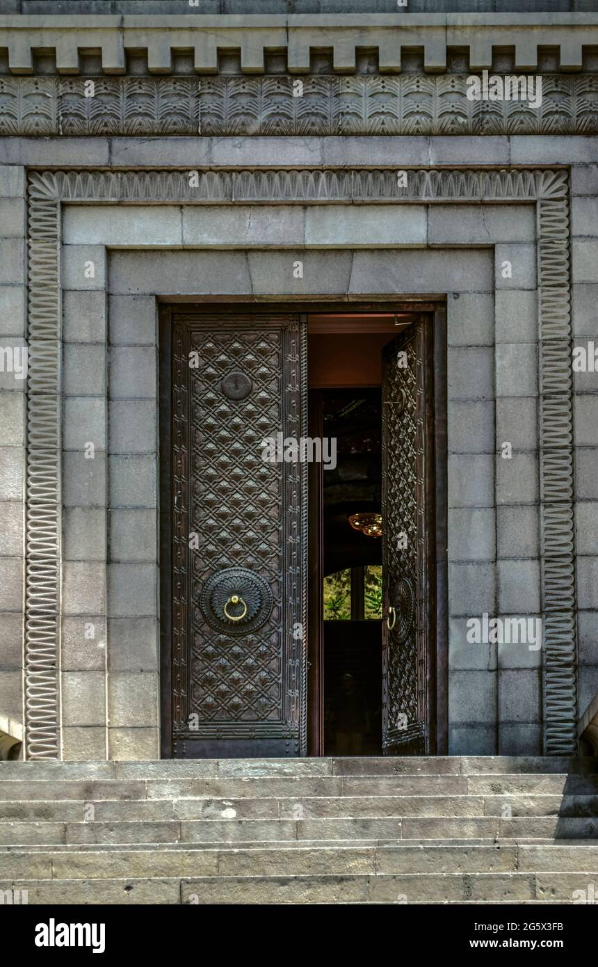 Huge front double-leaf, forged black door with a beautiful pattern and golden door handles, framed by a carved pattern on the wall of the basalt facad Stock Photo