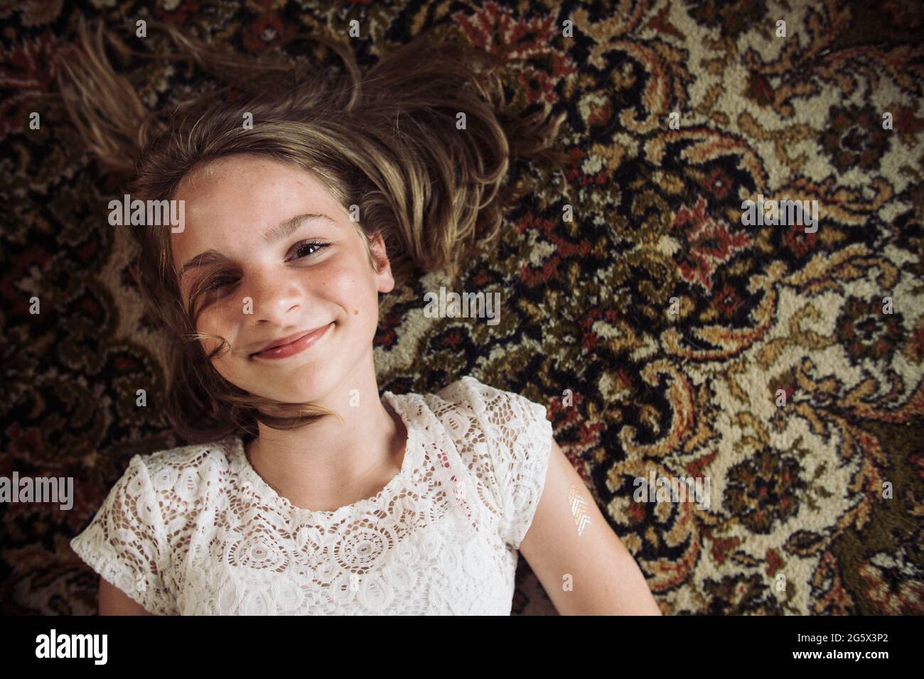 Smiling girl laying on the floor on a Persian carpet in a white dress. Stock Photo