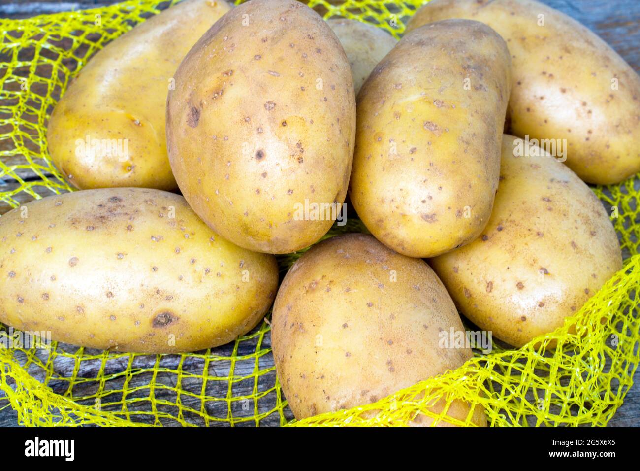 Heap of raw potatos in yellow string bag, on wooden background. Close-up. Studio photography. Stock Photo