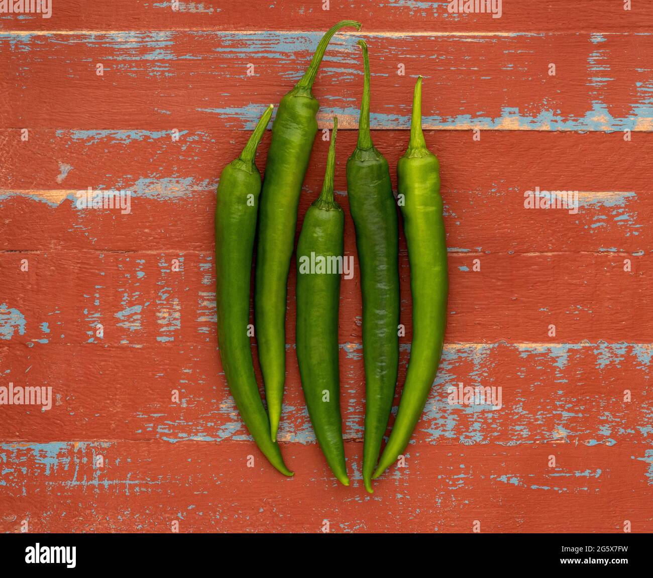 Plan view of green chilli peppers on a brown and blue  wooden background. Stock Photo