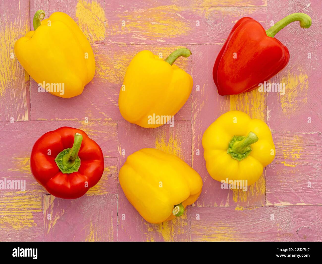 Plan view of red and yellow bell peppers on a pink and yellow  wooden background. Stock Photo