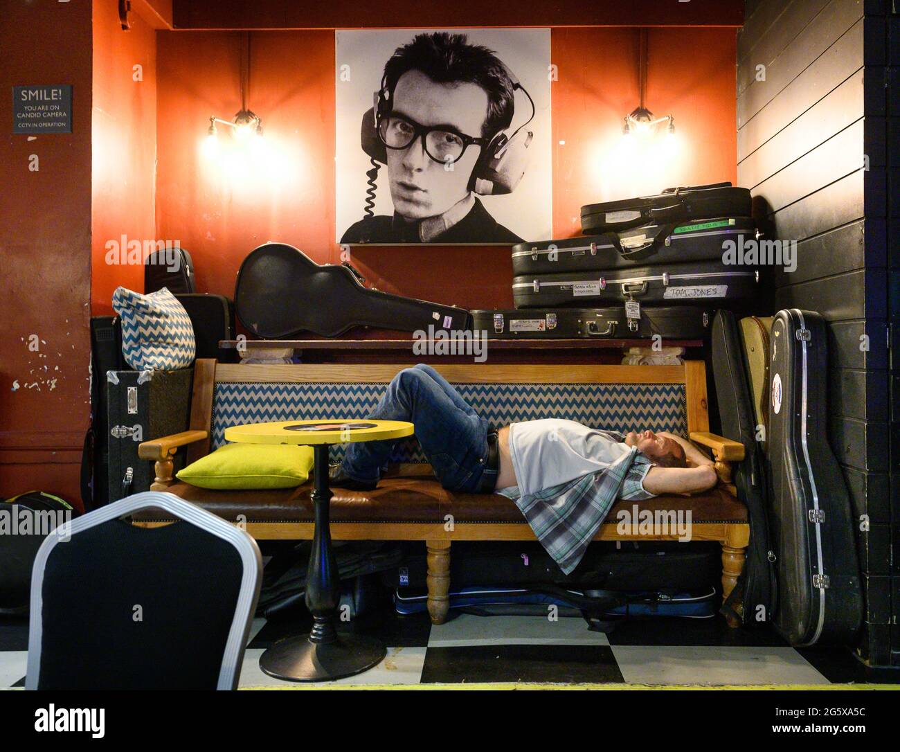 Band member of Los Pacaminos asleep under pic of Elvis Costello after live music gig at London Half Moon Putney pub. Stock Photo