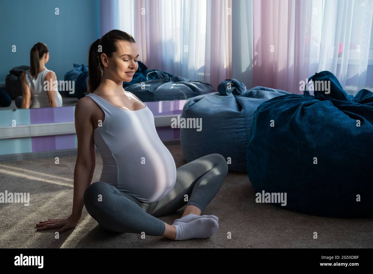 Happy pregnant woman practice yoga. A girl in the third trimester leads Pilates. Classes to prepare for childbirth. Waiting for the baby. Appeasement. Stock Photo