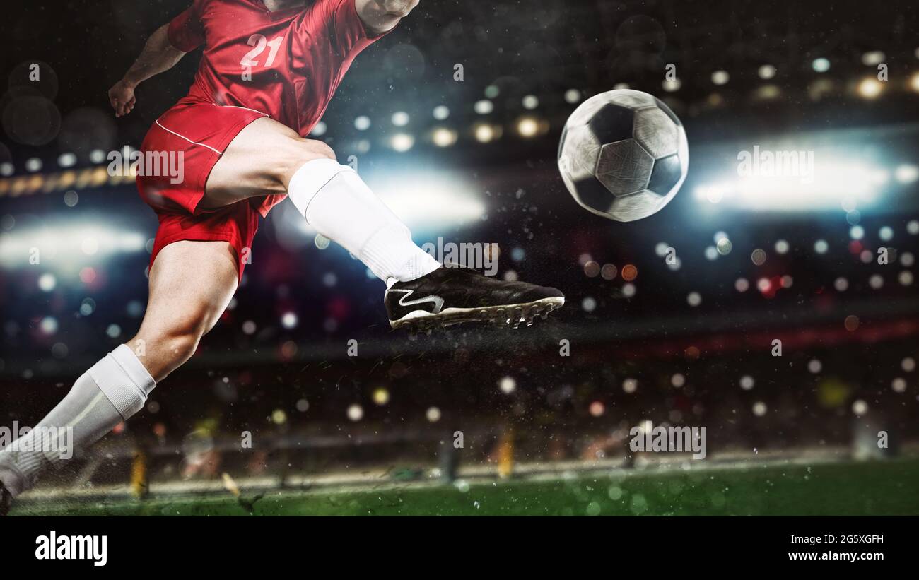 Close up of a soccer scene at night match with player in a red uniform kicking the ball with power Stock Photo
