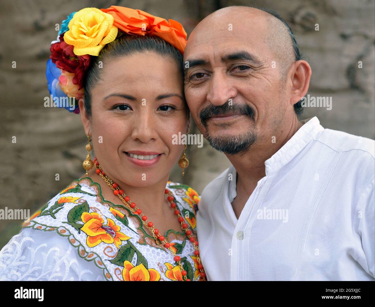 Dressed up Mexican Yucatecan couple (man and woman) with traditional hairstyles wears folkloric clothing and smiles for the camera. Stock Photo