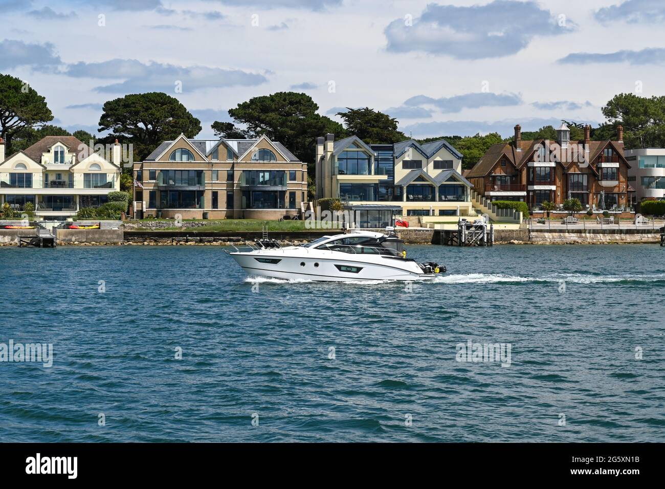 Poole, England - June 2021: Motorboat sailing past houses on the waterfront in the Sandbanks areas of Poole Stock Photo