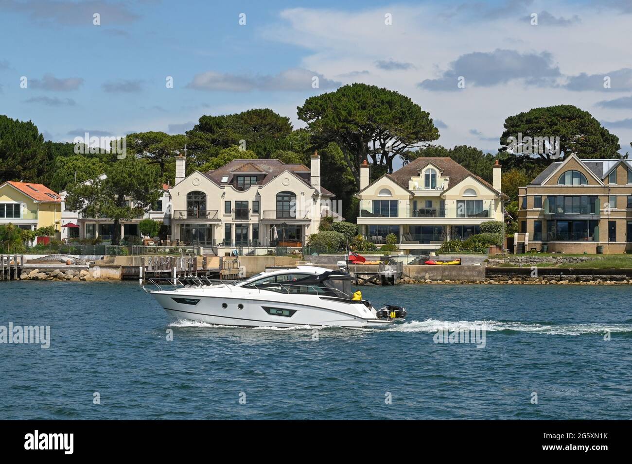 Poole, England - June 2021: Motorboat sailing past houses on the waterfront in the Sandbanks areas of Poole Stock Photo