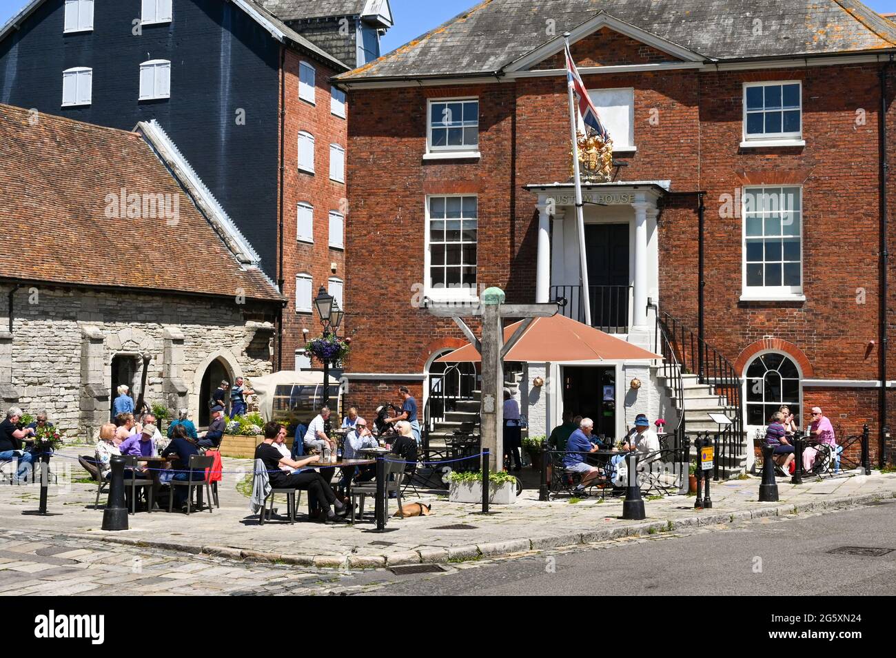 Poole, England - June 2021: People sitting outside the Custom House pub on the waterfront in Poole in summer sunshine Stock Photo