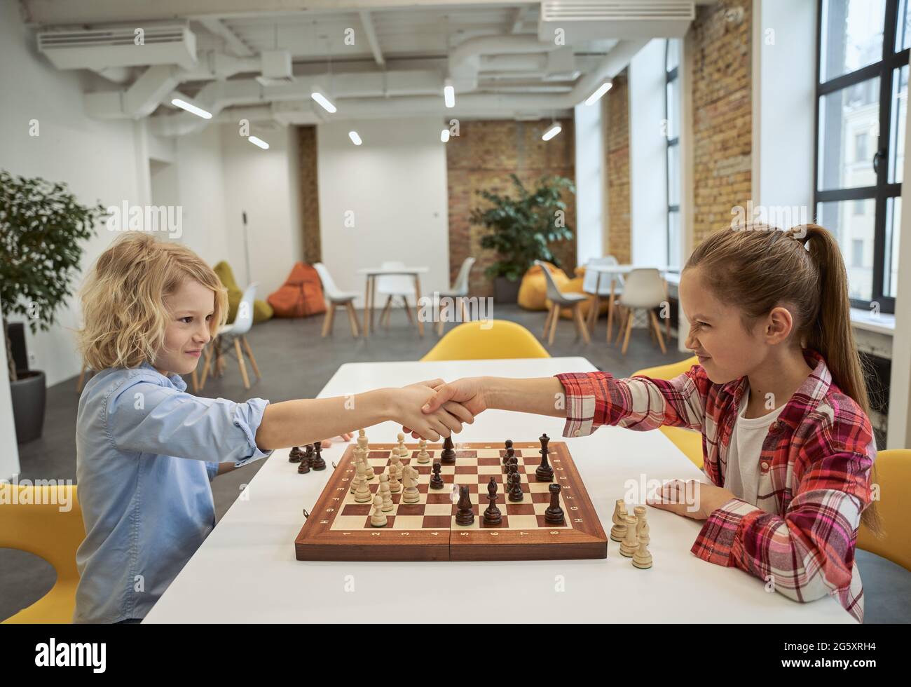 Rivalry. Two little children, boy and girl shaking hands after match, playing board game, sitting together at the table in school Stock Photo
