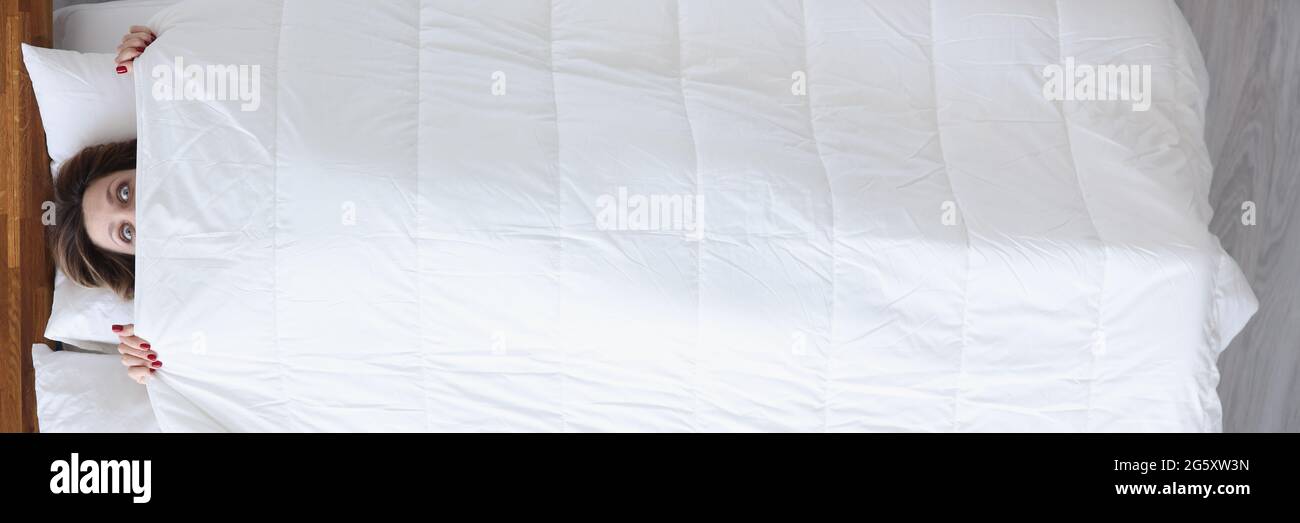 Woman with mad eyes looks out from under covers Stock Photo