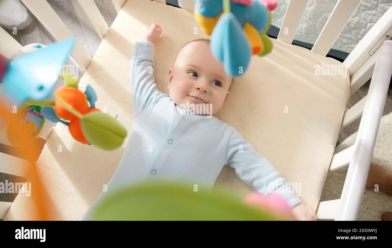Cute little baby lying in crib and looking on hanging colorful toys