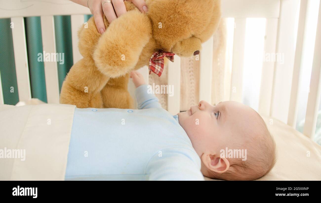 Young mother playing with teddy bear and her little baby boy lying in ...