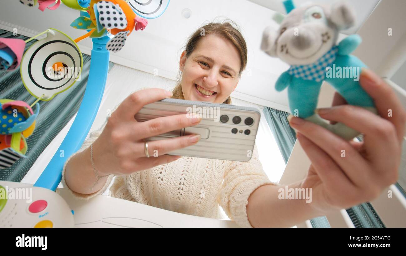 Smiling young mother shaking rattle toy to her baby and making ...