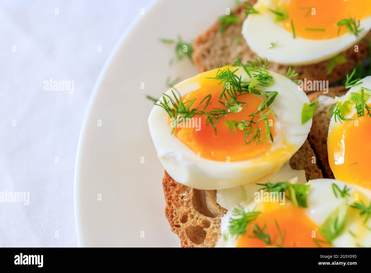 Soft-boiled egg halves with dill on whole grain toast bread on a white plate. Close-up, top view. Healthy, healthy and healthy breakfast concept Stock Photo