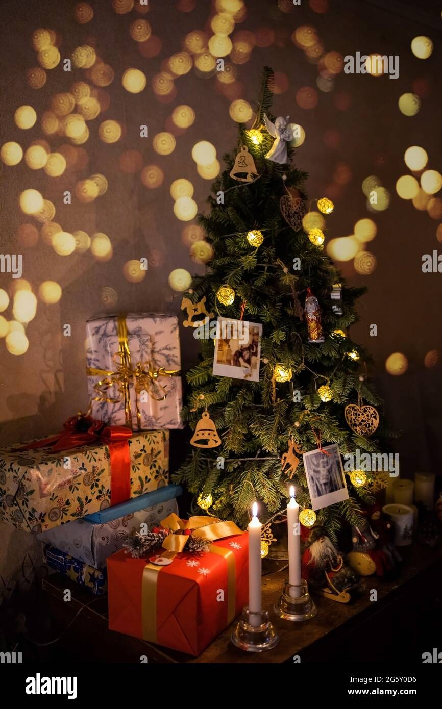beautiful wrapped boxes with gifts near the Christmas tree, there are candles, lights nearby, family photos and a garland are hanging on the tree. Stock Photo