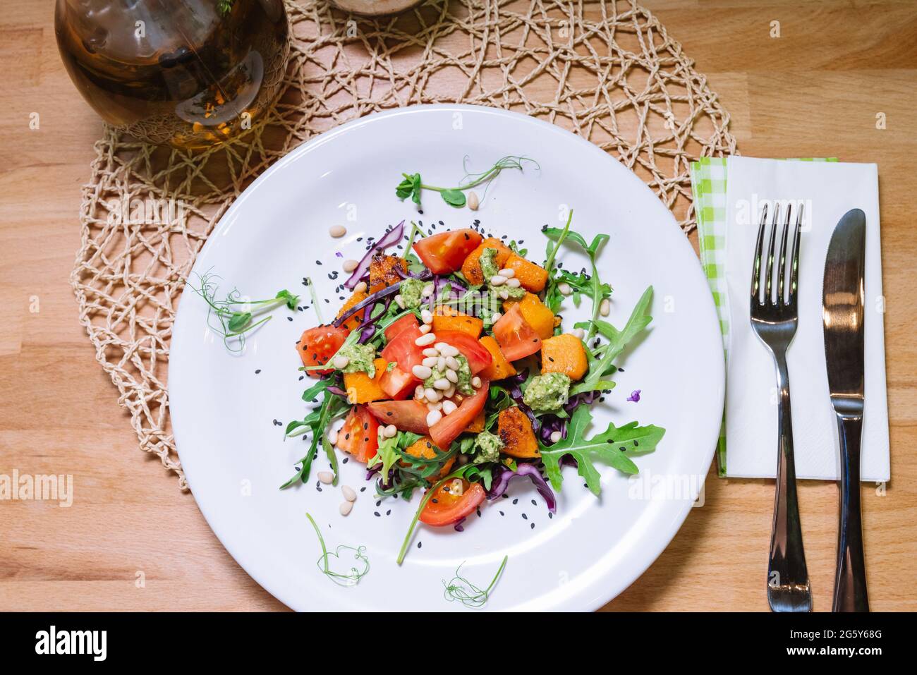 Warm salad with pumpkin, tomatoes, arugula, pesto sauce with pine nuts and black sesame seeds on white plate top view Stock Photo