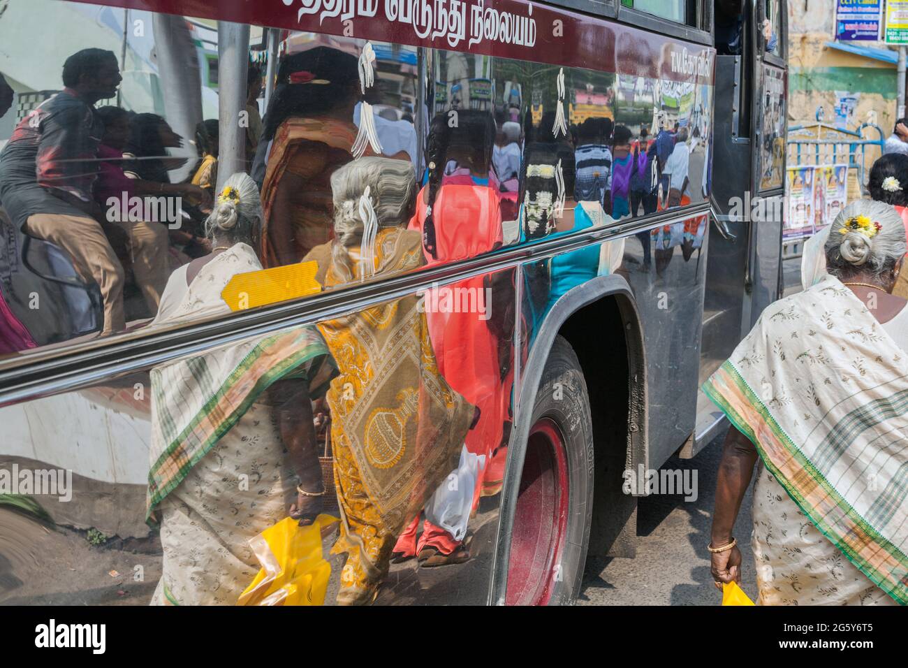 Reflection on silver bus of Indian passenger wearing sari walking past bus at Indian bus stand, Trichy, Tamil Nadu, India Stock Photo