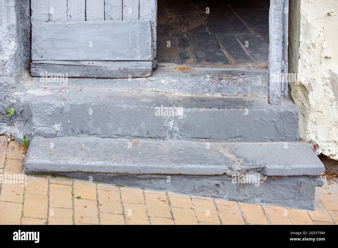 concrete steps entrance to the old house with a wooden door threshold of the building on the descent of the pedestrian sidewalk from stone tiles close Stock Photo