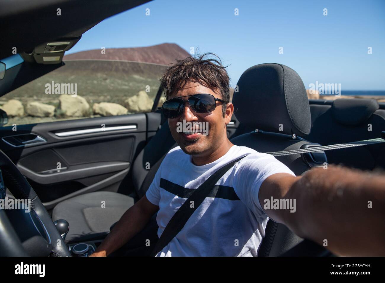 Smiling Indian man sitting in his convertible car takes a selfie, he is smiling and happy, wearing sunglasses. Successful man Stock Photo