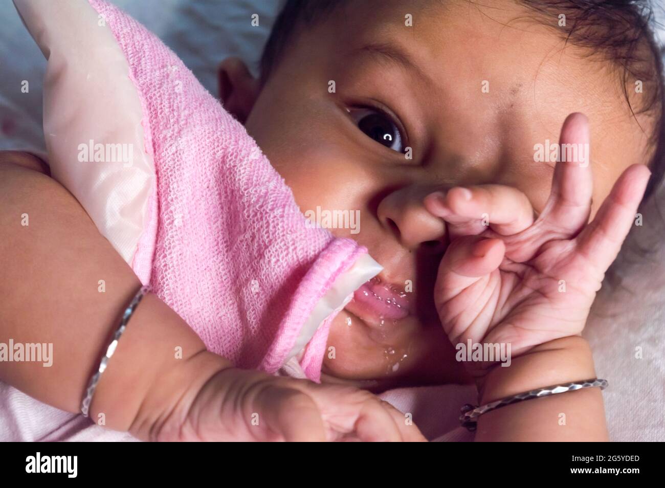 Cute baby boy wearing Baby Bib with Hands Covering Mouth while yawning in sleep and looking at camera. Sweet little infant toddler. Closeup portrait. Stock Photo