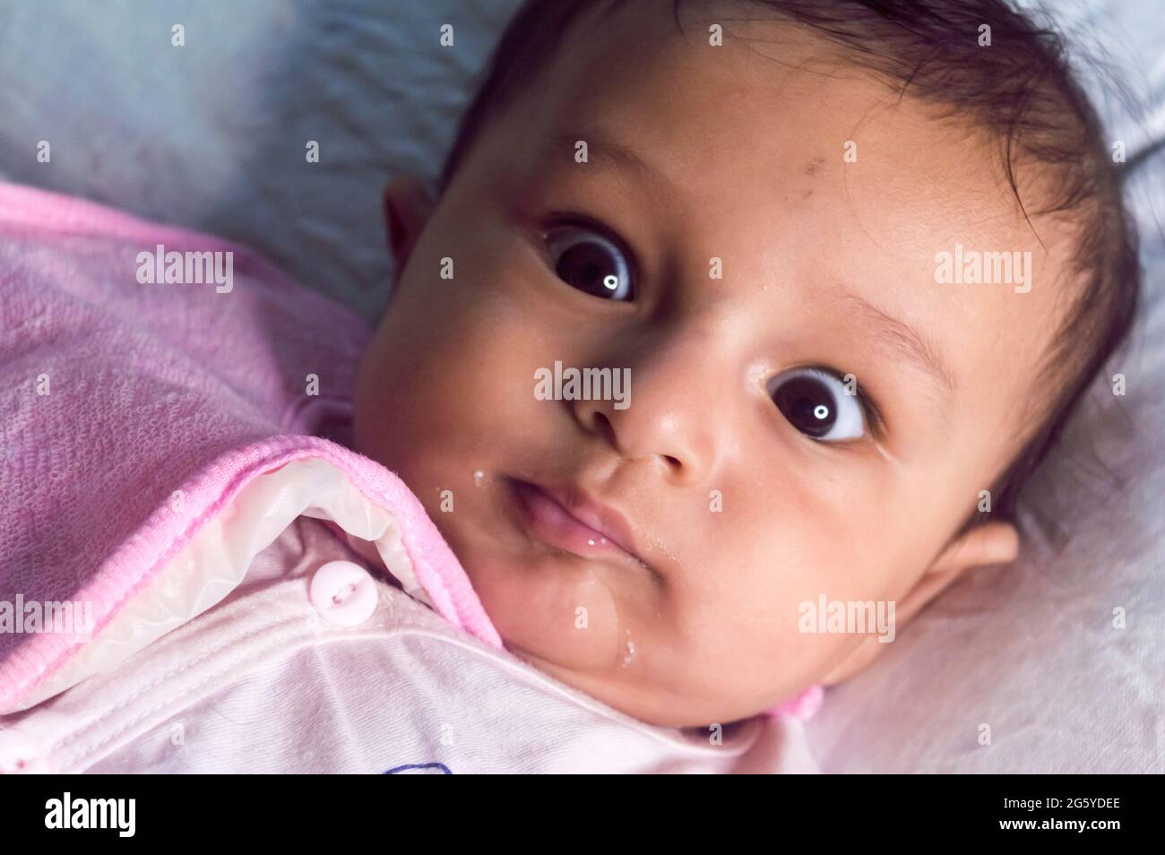 Cute baby boy wearing Baby Bib with beautiful Rolling Eyes lying on bed posing smiling and looking at camera. Sweet little infant toddler Closeup port Stock Photo