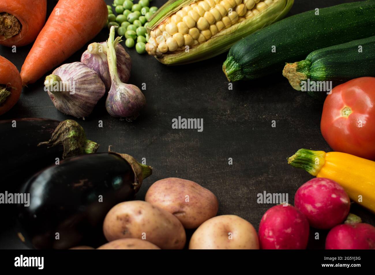 Corn, tomatoes, carrots, potatoes, eggplants, radishes and other vegetables on a black wooden table Stock Photo