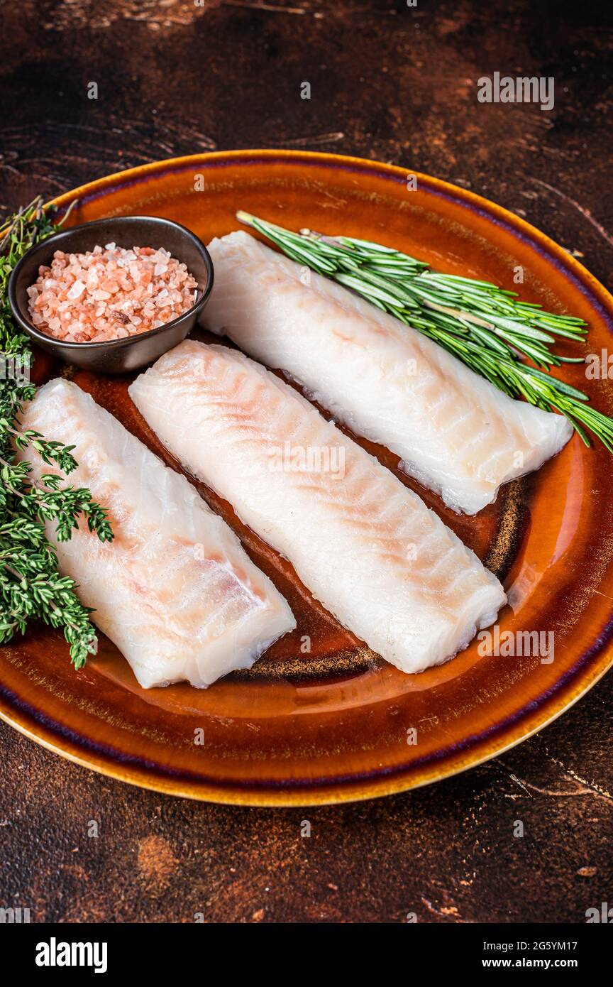 Raw Haddock loin fillet fish on rustic plate with thyme and salt. Dark