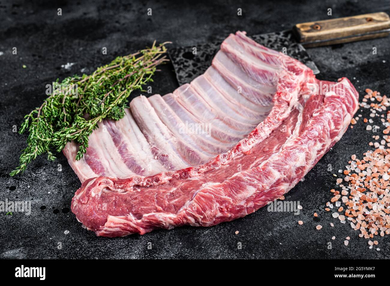 Lamb Rib Rack Cut Raw rack of lamb ribs on butcher cutting board with herbs. Black ...