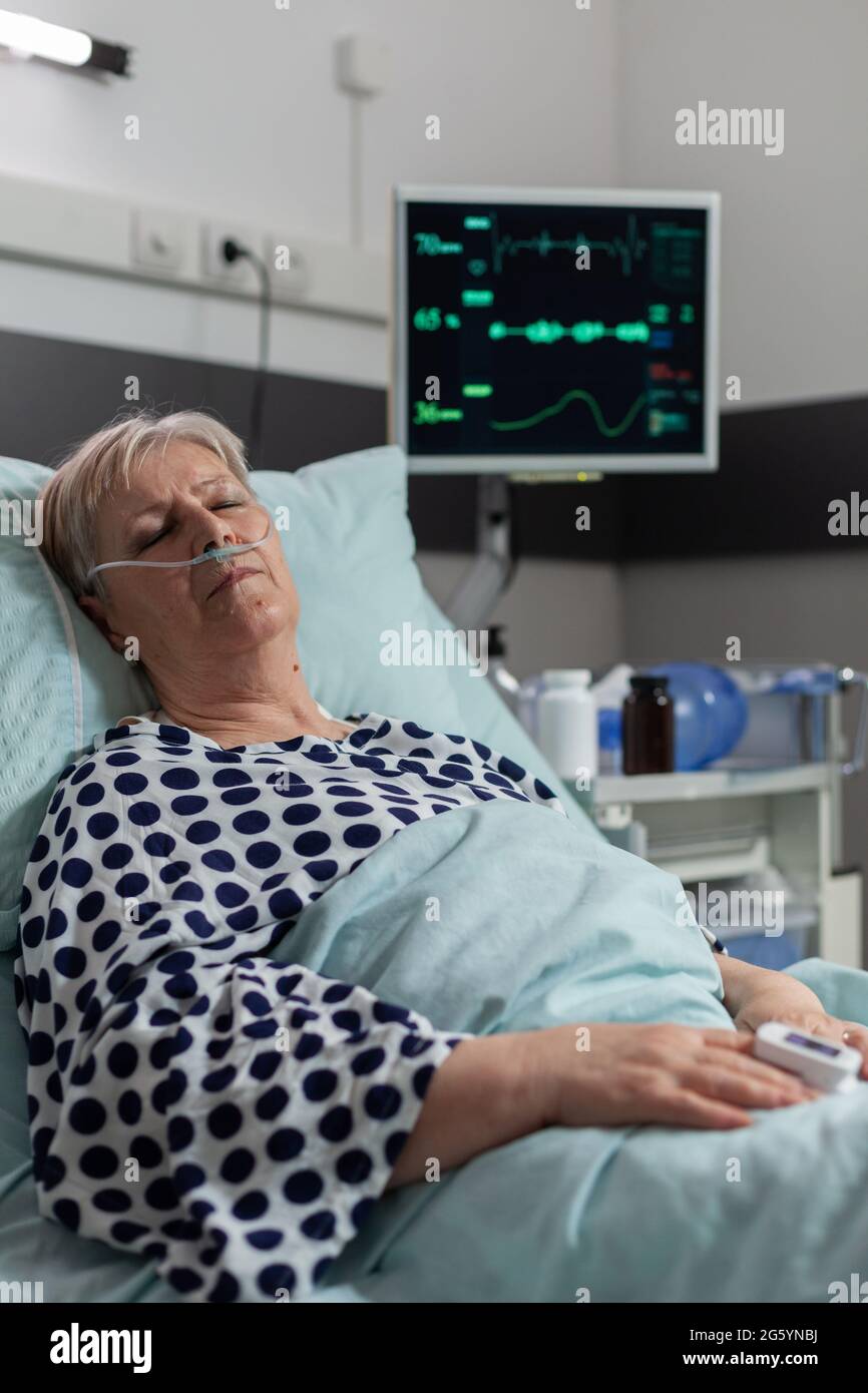 Senior woman patient laying in hospital bed with oxymeter attached on body, measuring oxygen saturation from blood and blood pressure and bmp. Getting treatment from iv drip bag. Stock Photo
