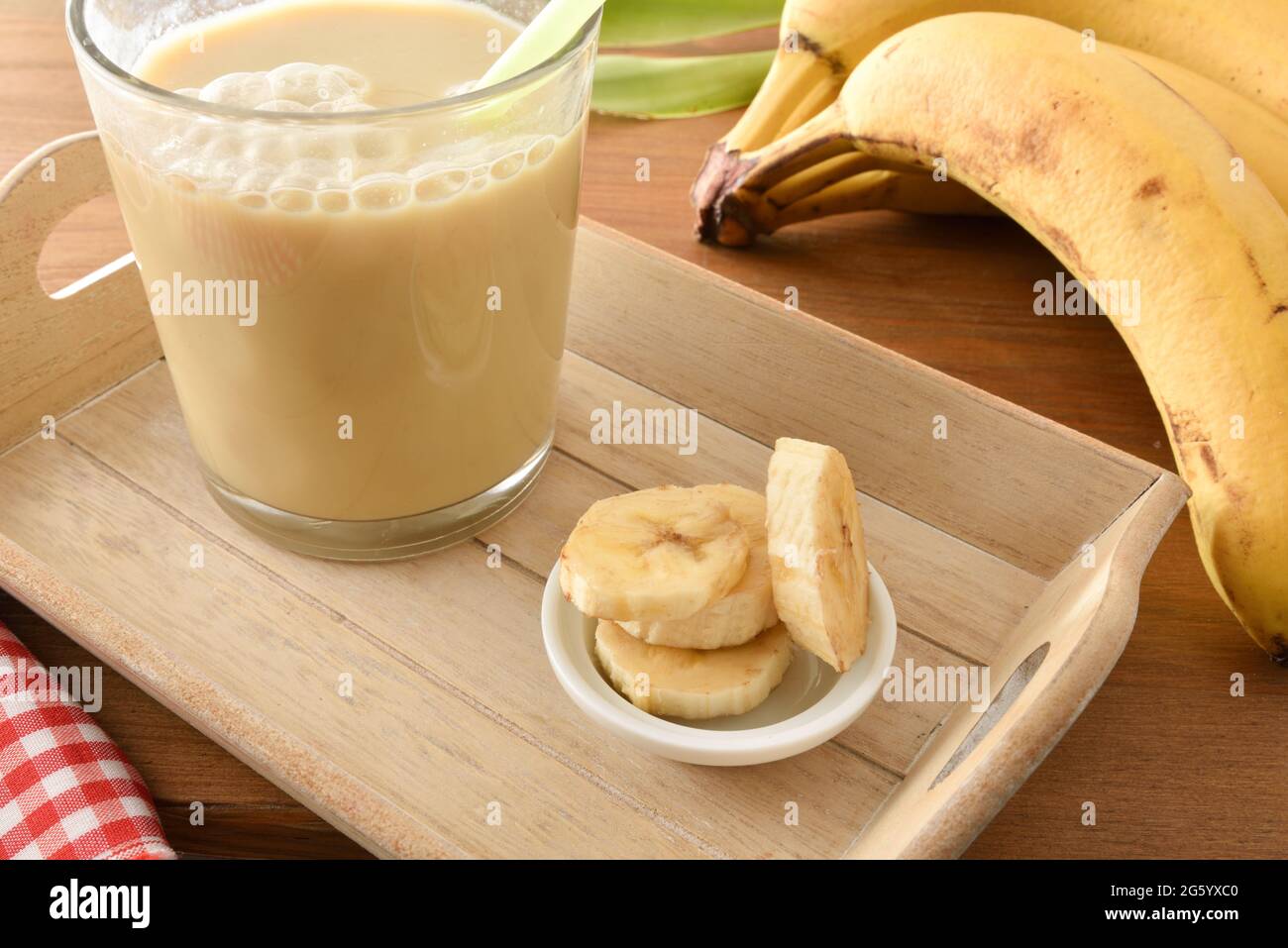 Banana drink with milk in glass on tray with fruit around and wooden table. Elevated view. Stock Photo