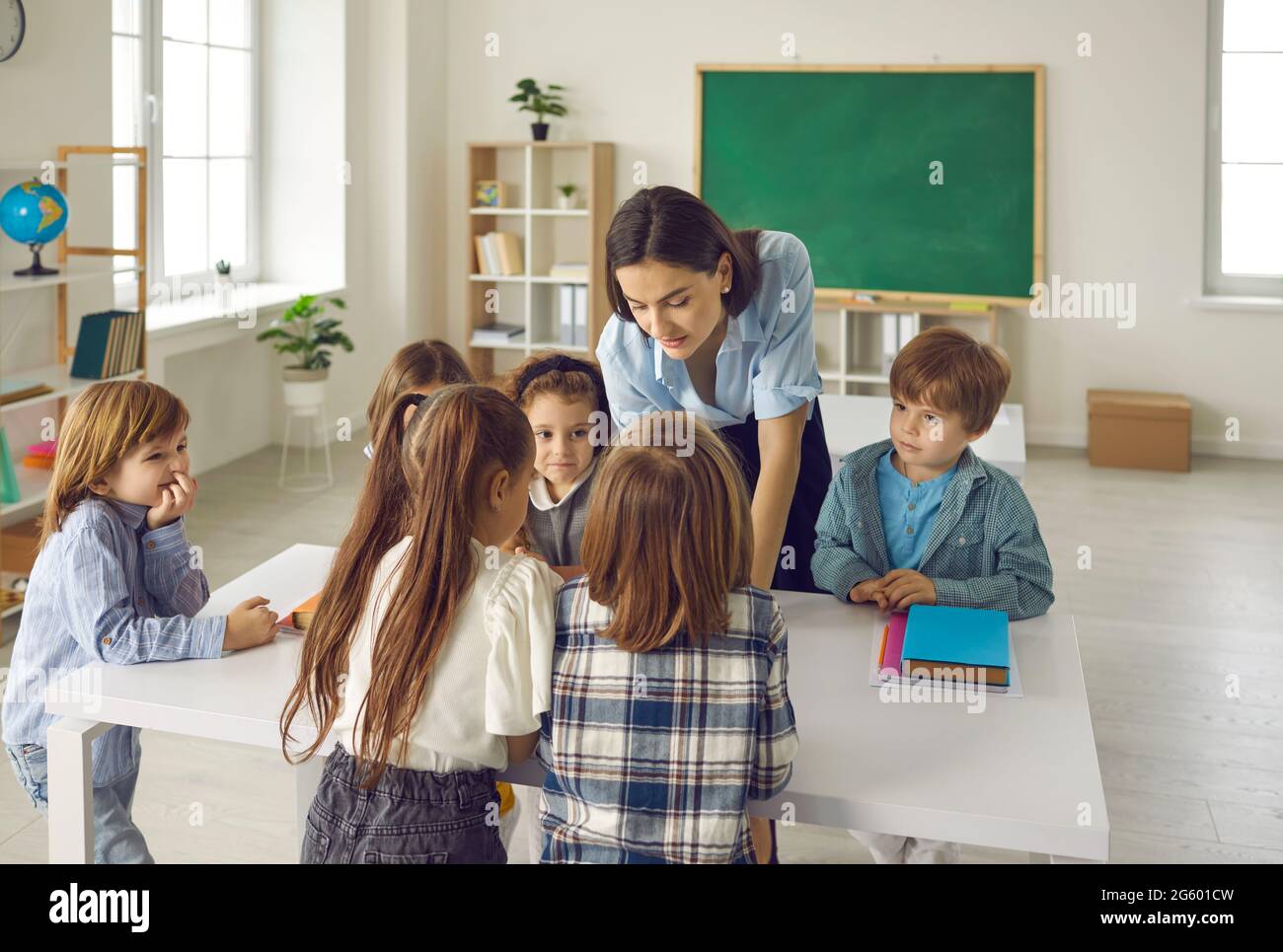 Group of children complete a task together with a young female primary school teacher. Stock Photo