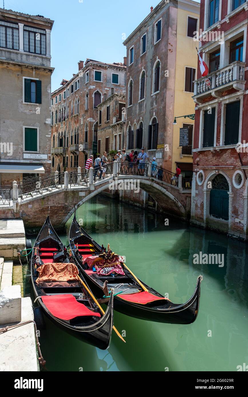 Tourists walking over a small bridge close to the moored gondolas on the Rio de S.Luca, one of the many inland canals in Venice, Italy Stock Photo