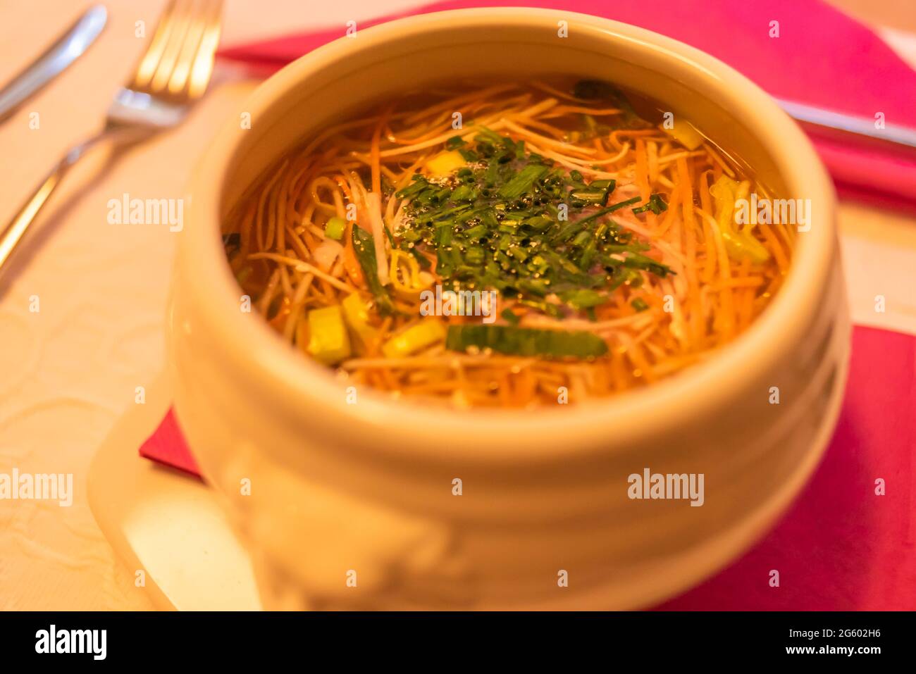 Noodle soup with green onion in a ceramic bowl, on red napkin. Stock Photo