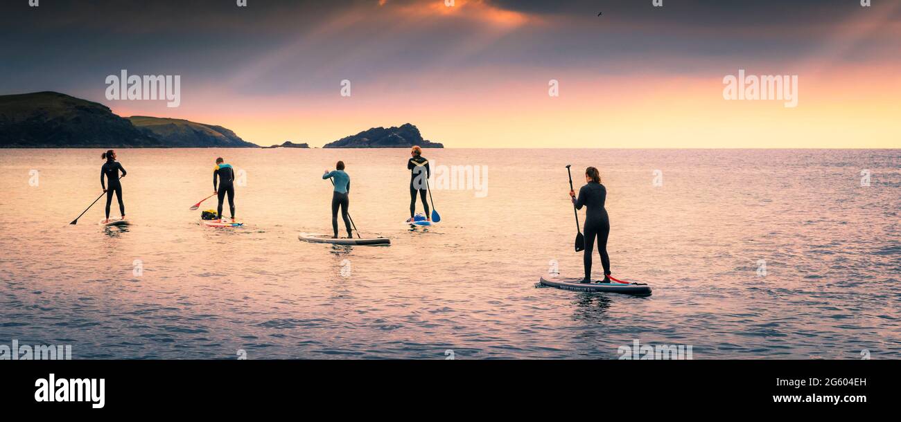 A panoramic image of a group of Stand Up Paddleboarders paddling across Fistral Bay in evening light at Newquay in Cornwall. Stock Photo