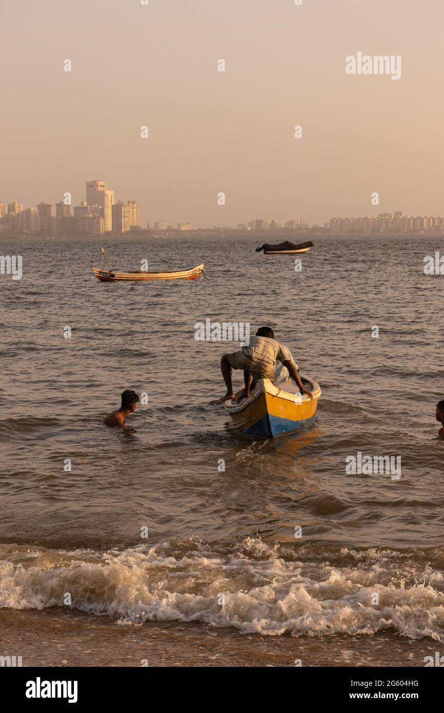 A fisherman climbing his boat and pushing it to sea at Marin drive beach at Mumbai India on 2 April 2021 Stock Photo