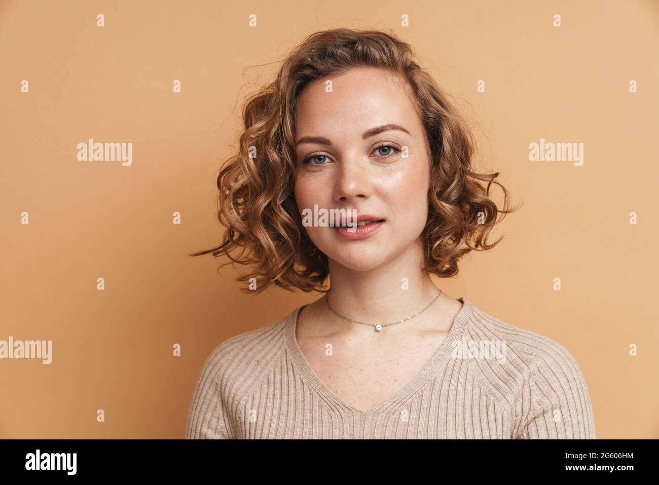 Young ginger woman with wavy hair posing and looking at camera isolated ...